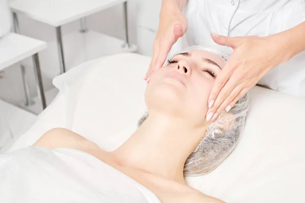 Beautician massages woman face skin for rejuvenation, anti aging skincare cosmetic procedure in beauty spa salon. Cosmetologist making facial massage with circular movements for beautiful female face