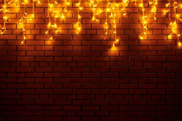 夜に赤レンガの壁からぶら下がる黄色いライトガーランド 魔法の休日の雰囲気と美しいクリスマスの家の装飾 壁に明るい黄色のライトが付いているクリスマスのガーランドを祝います — ストック写真