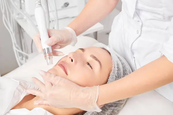 Cosmetologist makes aqua exfoliation for rejuvenation woman face skincare, anti aging cosmetic procedure in beauty spa salon. Beautician hands in gloves makes face skin treatment for tightening