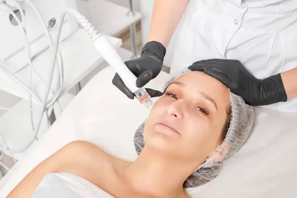 Cosmetologist makes aqua exfoliation for rejuvenation woman face skincare, anti aging cosmetic procedure in beauty spa salon. Beautician hands in black gloves makes face skin treatment for tightening