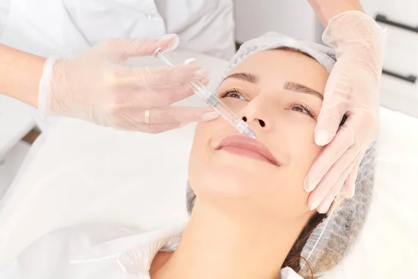Cosmetologist makes fillers injection for lips augmentation and volume, non surgical cosmetic procedure in beauty salon. Beautician specialist hands in gloves makes lips injection with syringe
