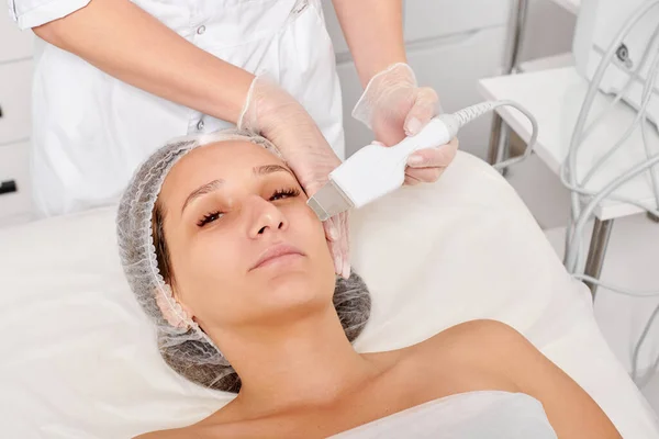 Cosmetologist makes facial ultrasonic peeling for rejuvenation woman face skincare, anti aging cosmetic procedure in beauty spa salon. Beautician makes face skin treatment with ultrasound scrubber