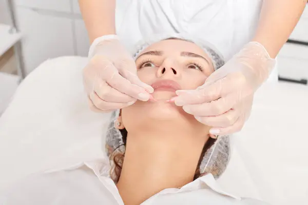 Cosmetologist applies facial oil capsules on woman face for rejuvenation, anti aging cosmetic procedure in beauty spa salon. Beautician hands in gloves holds oil capsules for nourishment