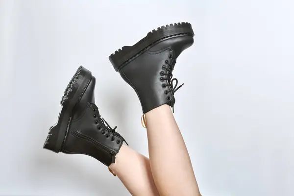 Woman legs in black combat boots on high heel platform with lug soles upside down side view on isolated white background. Female legs wear military fashionable high heel platform combat boots