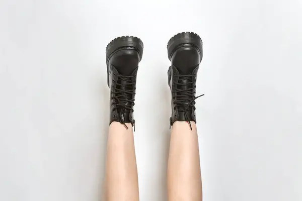 Woman legs in black combat boots on high heel platform with lug soles upside down, isolated white background. Female legs wear military fashionable high heel platform combat boots, new footwear trends