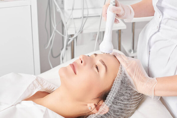 Cosmetologist makes RF lifting for rejuvenation woman face, anti aging cosmetic procedure in beauty spa salon. Beautician makes radio frequency treatment for collagen increasing on female face skin