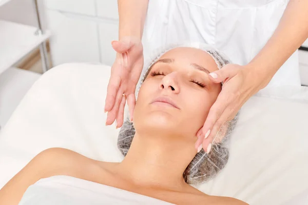 Beautician massages woman face skin for rejuvenation, anti aging skincare cosmetic procedure in beauty spa salon. Cosmetologist making facial massage with cosmetic cream for beautiful female face