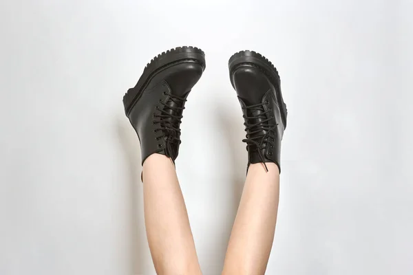 Woman legs in black combat boots on high heel platform with lug soles upside down, isolated white background. Female legs wear military fashionable high heel platform combat boots, new footwear trends