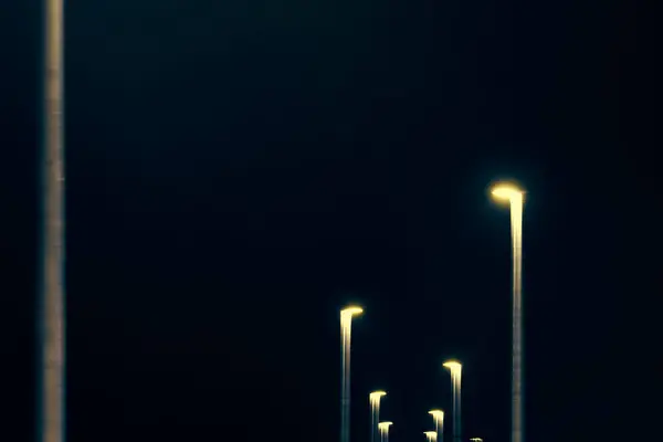 夜間のランプポストから黄色い点灯のぼやけたライン 青い緑色の夜の空の背景に抽象的な黄色の装飾的な都市ライト ブレイクされた黄色のストリートライト — ストック写真