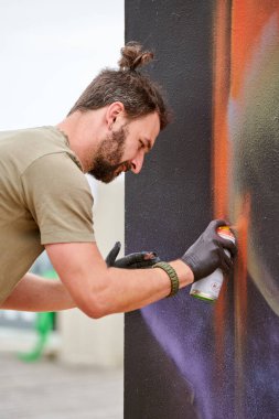Çekici erkek ressam, resim boyasını boya kutusuyla dış sokak sergisinde tuvale püskürtüyor.