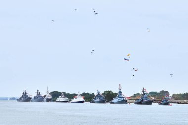 Airborne forces paratroopers flying Russian flag over naval forces parade warships along coastline, seafaring tradition of military ships formation at Navy Day, nautical spectacle of russian sea power clipart