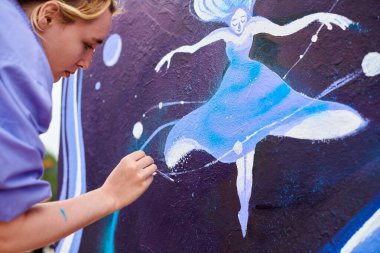 Kadın ressam, açık hava sokak sergisi için boya fırçasıyla resim çiziyor, kadın ressamın yan görüntüsünü kapatıyor fırça darbelerini tuvale uyguluyor, sanat yaratıcılığı senfonisi