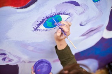 Kadın ressam, açık hava sokak sergisi için tuvale boya fırçasıyla resim çiziyor, kadın ressamın üst görüşünü kapatıyor, fırça darbelerini tuvale uyguluyor, sanat yaratıcılığı senfonisi
