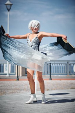 Uzay gümüş renkli mini etekli genç seksi bir kız. Performans yelpazesiyle dans ediyor. Zarif bir şekilde el sallıyor.