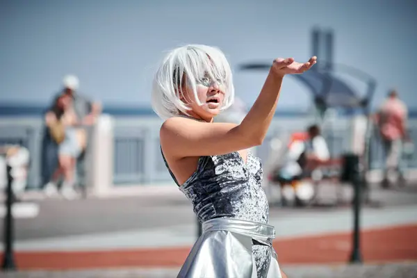 Stock image Young sexy girl in space silver micro skirt dancing with smooth, feminine and graceful movements, female outdoor dance performance on seaside promenade creating an arousing outdoor spectacle