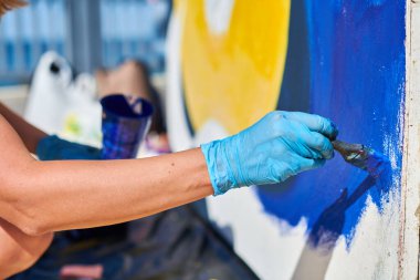 Kadın ressam eli, açık hava sokak sergisi için boya fırçasıyla canlı renkler kullanarak resim yapar, manzarayı kapatır