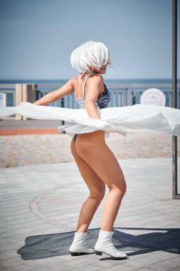 Beyaz ipek eşarpla dans eden, uzay gümüş renkli mini etekli genç seksi kız, deniz kenarında dans eden kadın, heyecan verici bir açık hava gösterisi yaratıyor.