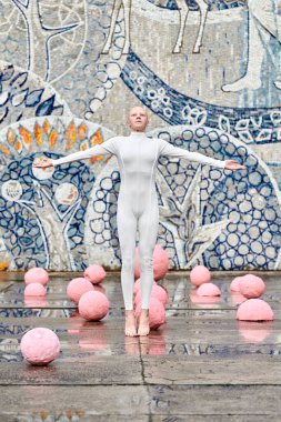 Beyaz fütüristik takım elbiseli genç tüysüz balerin kız balerin açık havada dans ediyor ve soyut mozaik Sovyet arka planında pembe küreler arasında zıplıyor, kendini ifade etmeyi simgeliyor.