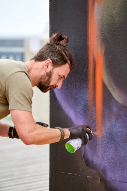 Çekici erkek ressam, resim boyasını boya kutusuyla dış sokak sergisinde tuvale püskürtüyor.