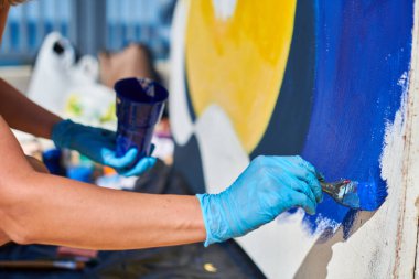 Kadın ressam eli, açık hava sokak sergisi için boya fırçasıyla canlı renkler kullanarak resim yapar, manzarayı kapatır