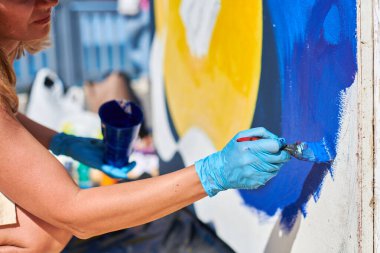 Kadın ressam eli, açık hava sokak sergisi için boya fırçasıyla canlı renkler kullanarak resim yapar, manzarayı kapatır