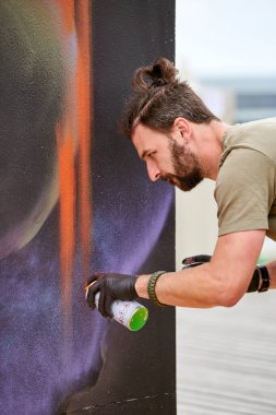 Çekici erkek ressam, resim boyasını boya kutusuyla dış sokak sergisinde tuvale püskürtüyor.