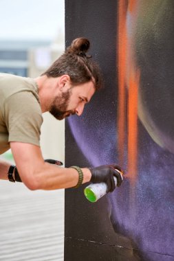 Çekici erkek ressam, resim boyasını boya kutusuyla dış sokak sergisinde tuvale püskürtüyor.