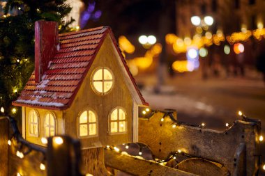 Gece vakti şehir sokağında sıcak camları olan Noel Masalı Evi, Yeni Yıl arifesinde festival şehir sokağının önünden geçen herkese sıcaklık ve neşe saçan kış mevsiminin ruhunu simgeler.