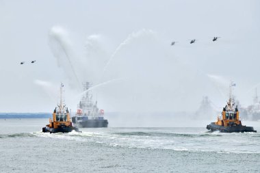 Rus deniz kuvvetleri boyunca yelken açan itfaiye teknesi kıyı şeridi boyunca askeri helikopterlerle savaş gemilerini geçit töreni, askeri gemilerin oluşumu denizcilik geleneği, Rus deniz gücünün deniz manzarası.