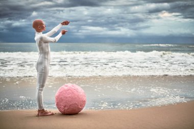 Pembe kürenin yanındaki deniz sahilinde duran beyaz fütüristik takım elbiseli tüysüz kızın tam boy portresi ve kollarını uzatarak, kel kızın metaforik gerçeküstü performansı umut yayıyor.