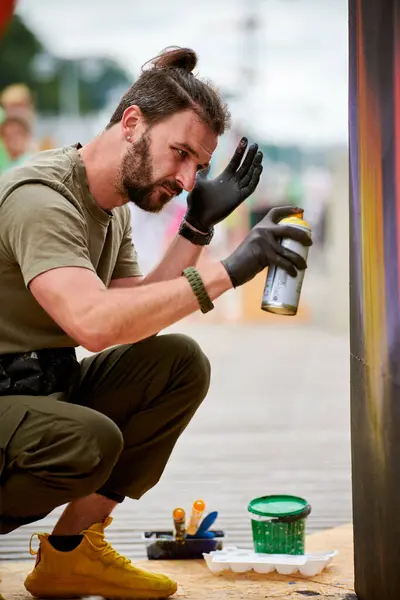 stock image Attractive male artist is painting picture with paint spray can spraying it onto canvas at outdoor street exhibition, side view of man art maker