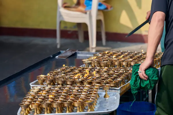 Nepalli tapınak personeli, fitil yandıktan sonra yenisi için mum yağı dökerek bronz mum tutucuları yeniden kullanacak, gönüllü olarak Kathmandu 'daki Boudhanath Stupa tapınağında çalışacak.