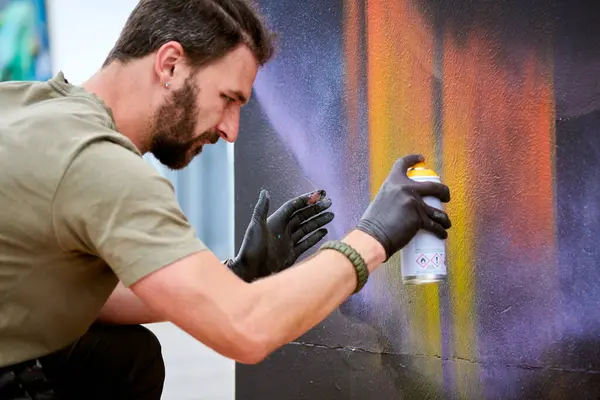 Çekici erkek ressam, resim boyasını boya kutusuyla dış sokak sergisinde tuvale püskürtüyor.