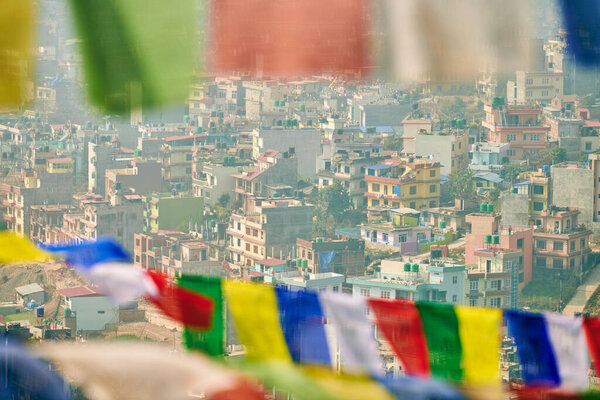 View of Kathmandu with lot of low rise buildings through colorful prayer flags, hilltop view of Kathmandu cityscape creating harmonious blend of spirituality and urbanity