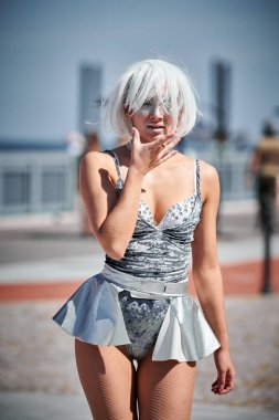 Uzay gümüş renkli mini etekli genç seksi kız pürüzsüz, kadınsı ve zarif hareketlerle dans ediyor. Sahilde dans eden kadın, heyecan verici bir açık hava gösterisi yaratıyor.