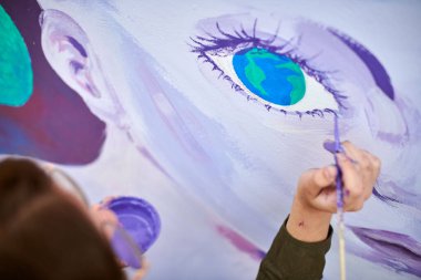 Kadın ressam, açık hava sokak sergisi için tuvale boya fırçasıyla resim çiziyor, kadın ressamın üst görüşünü kapatıyor, fırça darbelerini tuvale uyguluyor, sanat yaratıcılığı senfonisi
