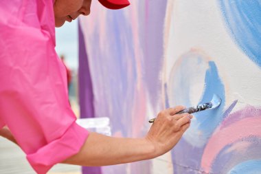 Şapkalı kadın ressam, açık hava sergisi için tuval üzerine fırçayla resim çiziyor, kadın ressamın yan görüntüsünü kapatıyor fırça darbelerini tuvale uyguluyor, sanat yaratıcılığı senfonisi