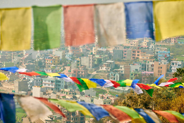 View of Kathmandu with lot of low rise buildings through colorful prayer flags, hilltop view of Kathmandu cityscape creating harmonious blend of spirituality and urbanity