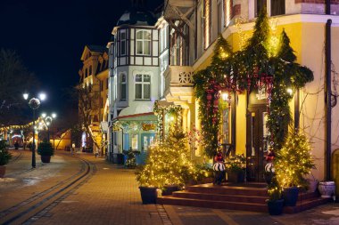 Zelenogradsk, Rusya - 09.01.2022 - Yeni Yıl dekorasyonları ve parıldayan çelenk gece lambalarıyla süslenmiş, caddeyi Noel harikalar diyarına çeviren Noel sıcaklığı ve bayram havası