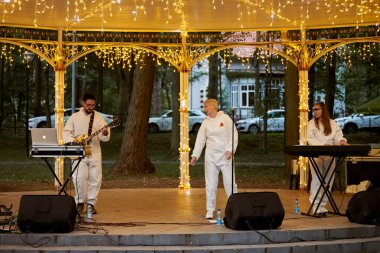 Svetlogorsk, Rusya - 13.08.2023 - Şehir parkının çardağında yerel pop rock müzik grubu, park ışıklarında klavyeci, gitarist ve vokalistin enerjik açık hava performansı