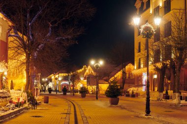 Zelenogradsk, Rusya - 09.01.2022 - Yeni Yıl dekorasyonları ve parıldayan çelenk gece ışıkları ile süslenmiş Noel caddesi gece şehrinin büyülü neşeli atmosferini yaratıyor