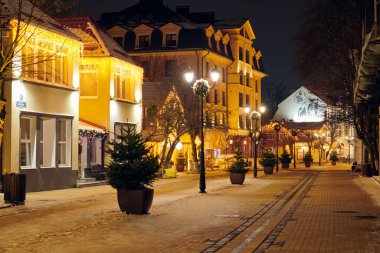 Zelenogradsk, Rusya - 09.01.2022 - Yeni Yıl dekorasyonları ve parıldayan çelenk gece ışıkları ile süslenmiş Noel caddesi gece şehrinin büyülü neşeli atmosferini yaratıyor