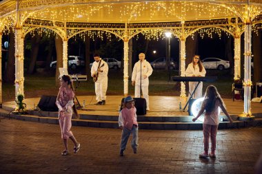 Svetlogorsk, Rusya - 13.08.2023 - Yerel pop rock müzik grubu şehir parkının çardağında, dans pistinde dans eden mutlu çocuklar, park ışıklarında dans ederken