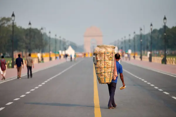 stock image New Delhi, India - 23.10.2022 - Indian street vendor of puri carrying large basket behind his back with poori deep fried bread, street huckster walks on Rajpath boulevard in New Delhi