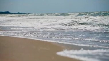 Görkemli okyanus dalgaları kumlu sahile çarpıyor berrak gökyüzü altında, alçak açı manzaralı