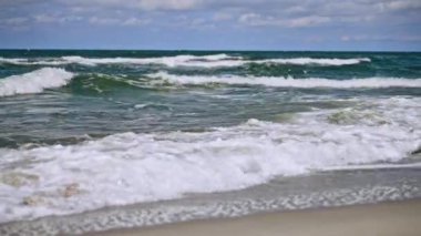 Sakin okyanus dalgaları bulutlu gökyüzünün altında kumlu kıyılara çarpıyor.