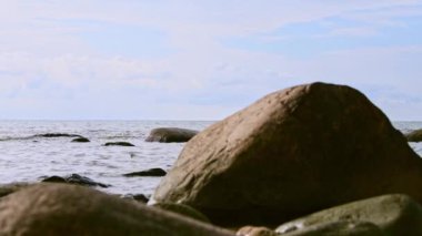 Geniş gökyüzünün altında kıyı boyunca dağılmış büyük kayalıklarla sakin bir sahil manzarası. Huzur ortamı, yumuşak dalgalarla geliştirilmiş sükunet ve zamansızlığı çağrıştırır.