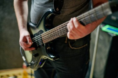 Müzik provasında elektro bas gitar çalan müzisyen, loş ayarlarda gitar tekniği pratik yapan, gitarist ellerini kapat