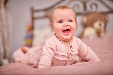 Açık renk saçlı, beyaz ırktan, pembe elbiseli, neşeli genç bir kadın. Ilık aydınlatma neşeli ifadeyi artırır. Yumuşak dekor samimi dokunuş ekler