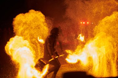 Gece gökyüzünde parıldayan iki itfaiyeci silueti, bir yangın gösterisi sırasında enerji ve ateş manipülasyonu gösteriyorlar.